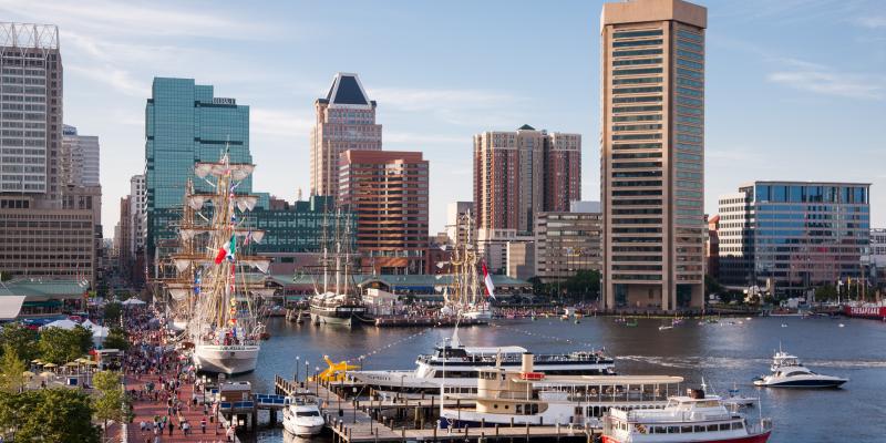 Historical tall ships in the Inner Harbor of Baltimore, Maryland, USA with the city's skyscrapers and buildings in the background.