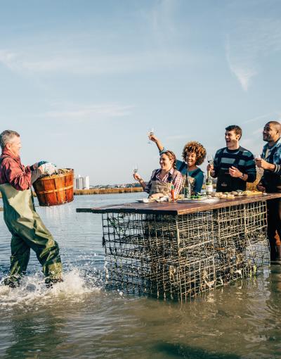 A waterman brings a basket of oysters to a group dining in the water