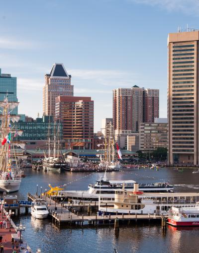Historical tall ships in the Inner Harbor of Baltimore, Maryland, USA with the city's skyscrapers and buildings in the background.
